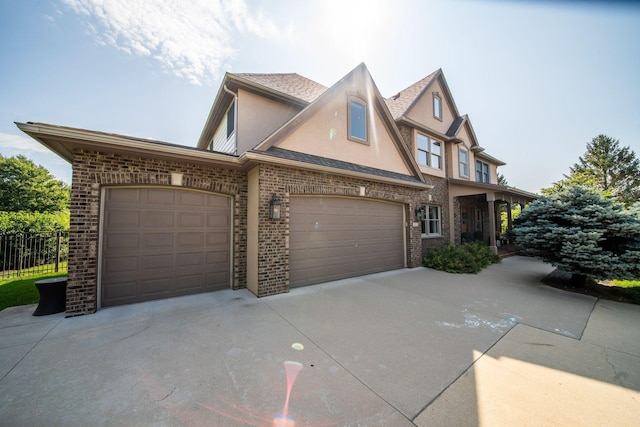 tudor house featuring fence, an attached garage, stucco siding, concrete driveway, and brick siding