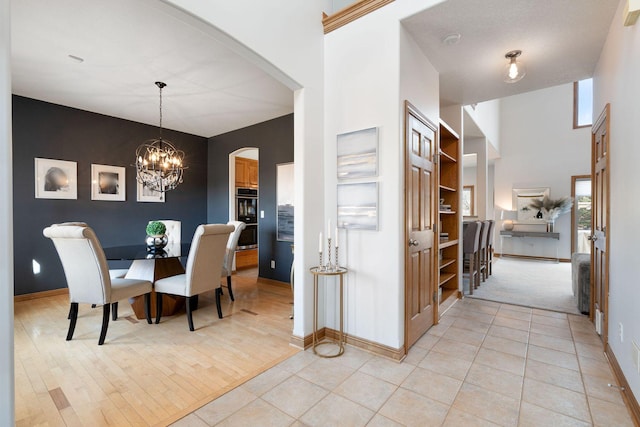 dining room with baseboards, a towering ceiling, light tile patterned flooring, arched walkways, and a notable chandelier