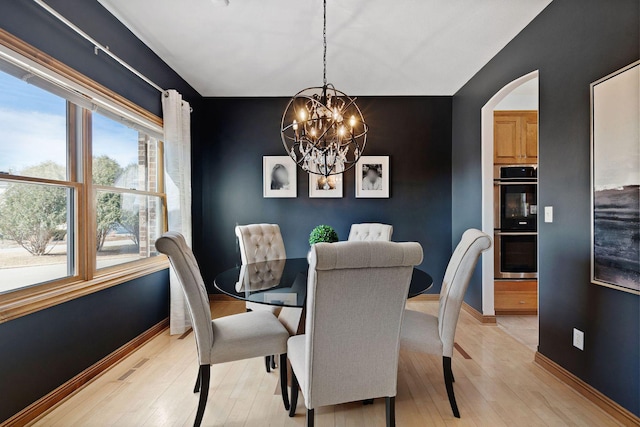 dining space featuring light wood-type flooring, baseboards, arched walkways, and an inviting chandelier