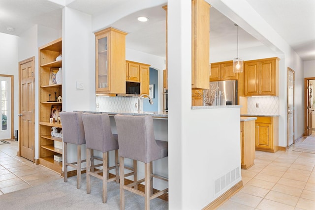 kitchen with light tile patterned floors, glass insert cabinets, a kitchen breakfast bar, and freestanding refrigerator