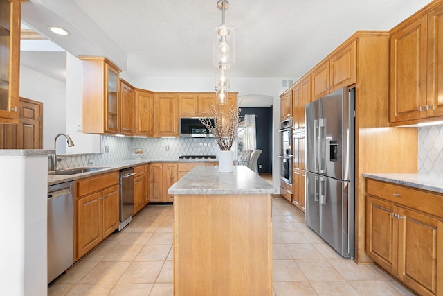 kitchen featuring a kitchen island, arched walkways, a sink, stainless steel appliances, and glass insert cabinets