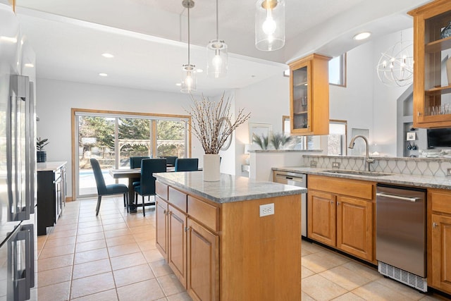 kitchen featuring light stone countertops, a sink, hanging light fixtures, stainless steel appliances, and a center island