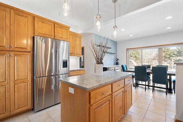 kitchen featuring light tile patterned floors, brown cabinetry, stainless steel fridge with ice dispenser, decorative light fixtures, and a center island