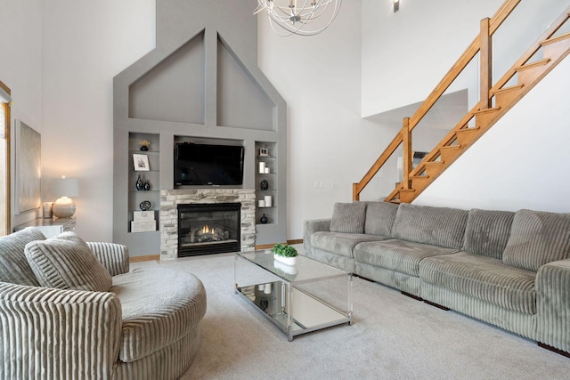 living area featuring built in shelves, carpet, stairs, a towering ceiling, and a glass covered fireplace