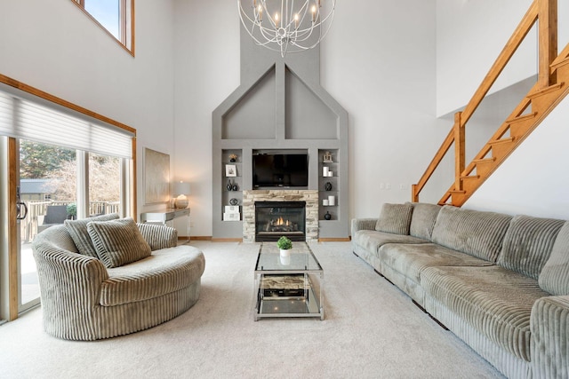 carpeted living area featuring a stone fireplace, stairway, plenty of natural light, and an inviting chandelier