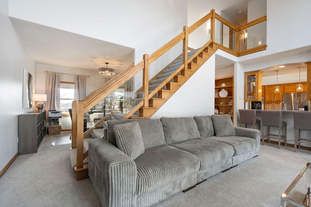 living room featuring light carpet, a notable chandelier, stairs, and baseboards