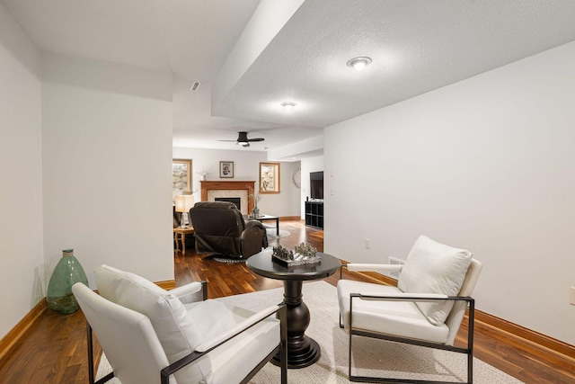 living room with a tiled fireplace, baseboards, a ceiling fan, and wood finished floors