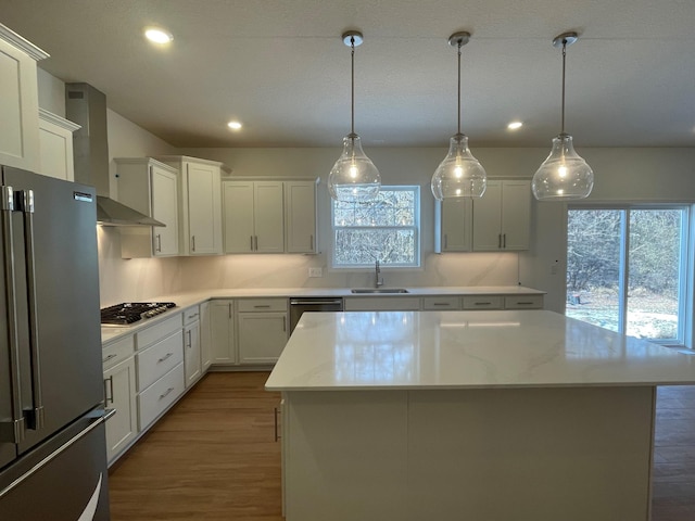 kitchen featuring pendant lighting, white cabinets, a center island, stainless steel appliances, and wall chimney exhaust hood