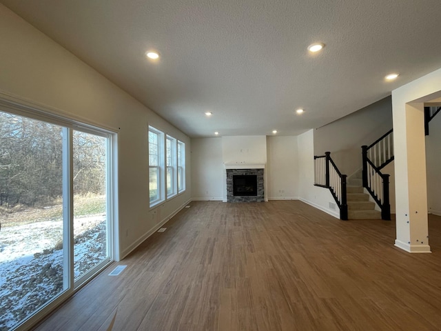 unfurnished living room with hardwood / wood-style flooring, a stone fireplace, and a textured ceiling