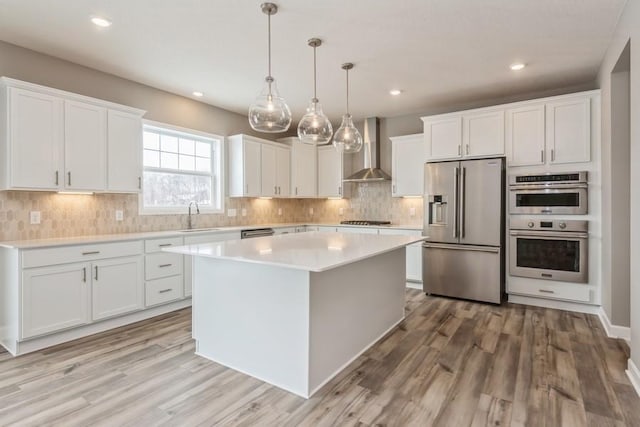 kitchen featuring white cabinetry, decorative light fixtures, appliances with stainless steel finishes, a kitchen island, and wall chimney range hood