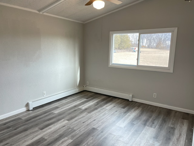 spare room featuring ceiling fan, a baseboard heating unit, wood-type flooring, ornamental molding, and vaulted ceiling