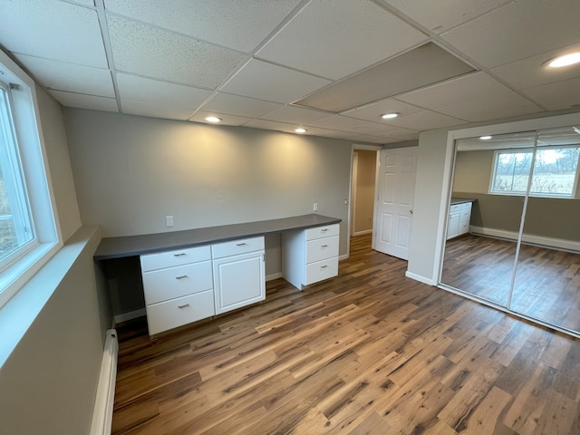 unfurnished office with a paneled ceiling, dark wood-type flooring, and built in desk