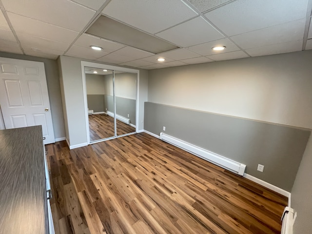 unfurnished bedroom featuring hardwood / wood-style flooring, a paneled ceiling, a closet, and baseboard heating