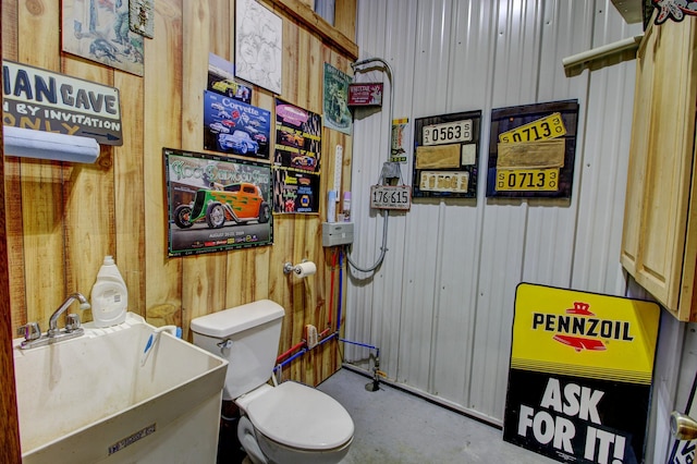 bathroom featuring a sink, concrete flooring, toilet, and wood walls