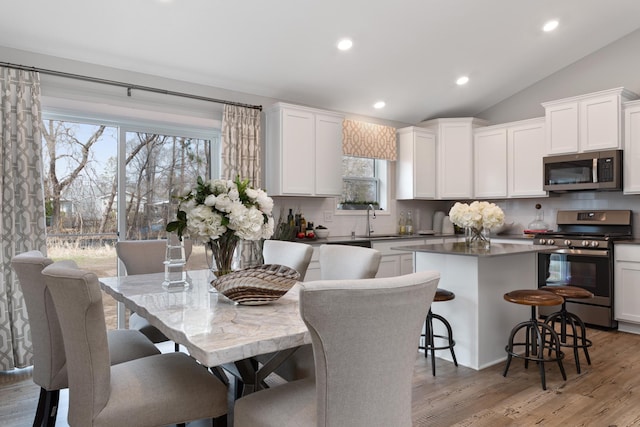 kitchen with a kitchen island, appliances with stainless steel finishes, lofted ceiling, backsplash, and a kitchen bar