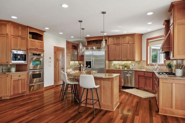 kitchen featuring hanging light fixtures, dark hardwood / wood-style floors, stainless steel appliances, light stone countertops, and a kitchen island with sink