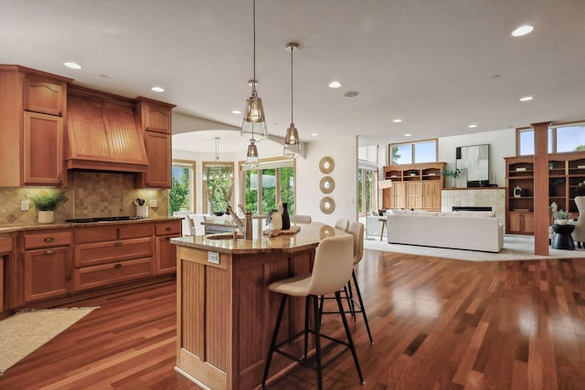 kitchen featuring premium range hood, a kitchen bar, sink, an island with sink, and pendant lighting