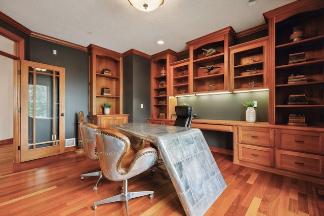 office space with hardwood / wood-style flooring, ornamental molding, built in desk, and a textured ceiling