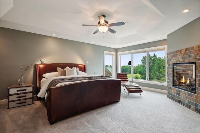 bedroom with a raised ceiling, a tiled fireplace, carpet flooring, and ceiling fan