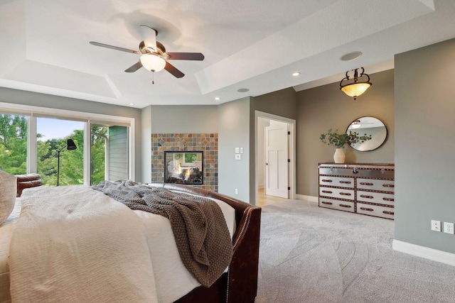 carpeted bedroom featuring a tiled fireplace, a raised ceiling, and ceiling fan