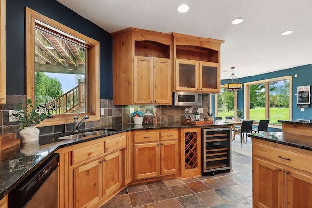 kitchen featuring sink, appliances with stainless steel finishes, decorative light fixtures, beverage cooler, and dark stone counters