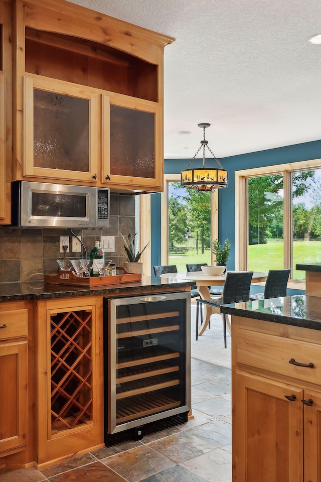 bar with pendant lighting, beverage cooler, backsplash, and dark stone counters