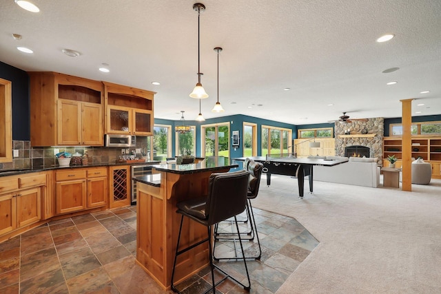 kitchen with a kitchen island, a stone fireplace, beverage cooler, a kitchen bar, and hanging light fixtures