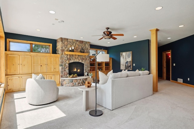 living room featuring ornate columns, a stone fireplace, light carpet, and ceiling fan