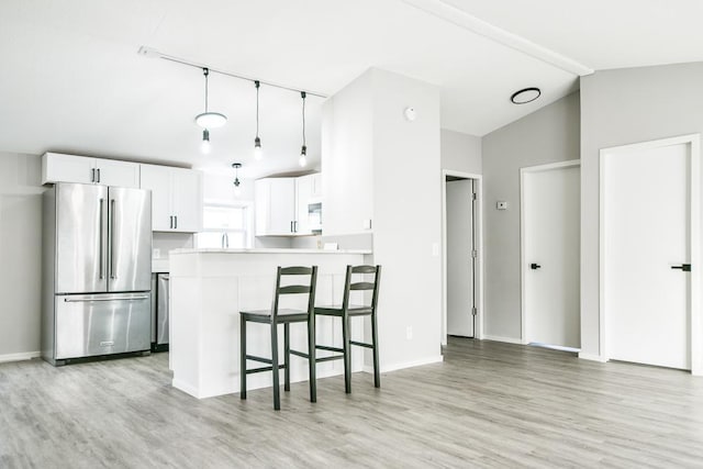 kitchen featuring lofted ceiling, a breakfast bar area, stainless steel refrigerator, white cabinetry, and kitchen peninsula