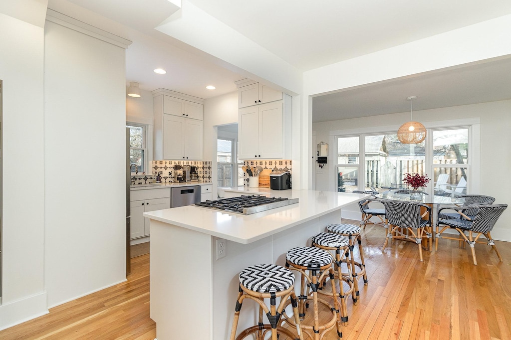 kitchen with appliances with stainless steel finishes, decorative light fixtures, white cabinets, a kitchen breakfast bar, and light hardwood / wood-style flooring