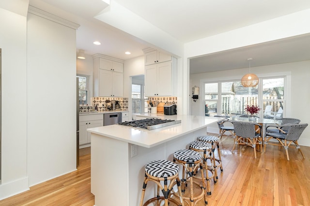 kitchen with appliances with stainless steel finishes, decorative light fixtures, white cabinets, a kitchen breakfast bar, and light hardwood / wood-style flooring