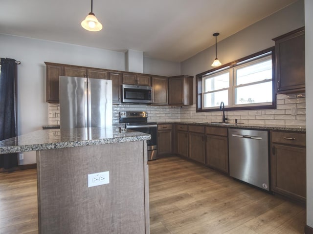 kitchen with a kitchen island, a sink, appliances with stainless steel finishes, dark stone counters, and decorative light fixtures