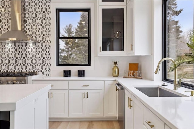 kitchen featuring dishwasher, white cabinetry, sink, and wall chimney range hood