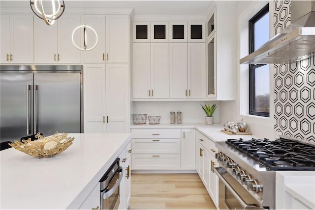 kitchen with white cabinetry, wall chimney range hood, hanging light fixtures, and high quality appliances