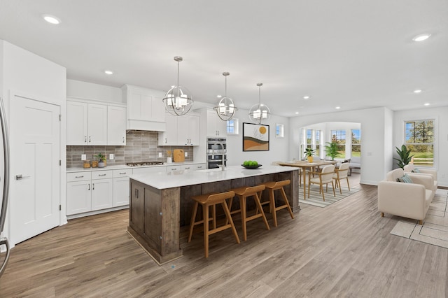 kitchen featuring stainless steel appliances, pendant lighting, a center island with sink, and white cabinets