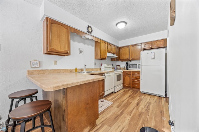 kitchen with sink, a kitchen breakfast bar, kitchen peninsula, white appliances, and light hardwood / wood-style flooring