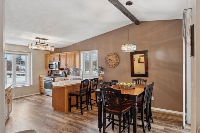 dining room with sink, light hardwood / wood-style flooring, and lofted ceiling with beams