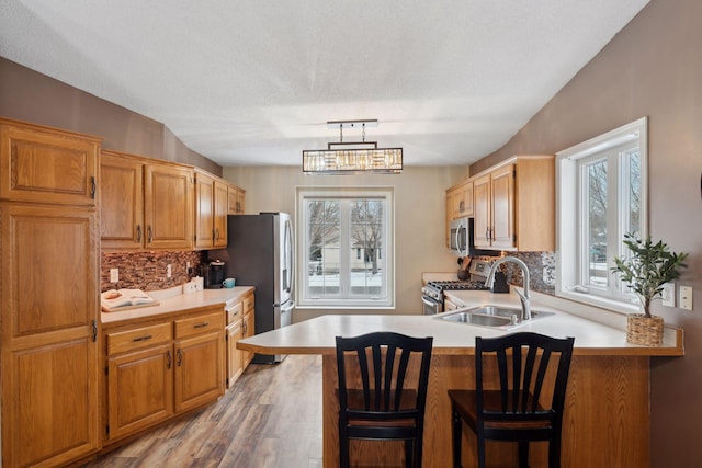 kitchen with appliances with stainless steel finishes, kitchen peninsula, hanging light fixtures, and backsplash