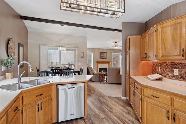 kitchen featuring decorative light fixtures, sink, hardwood / wood-style flooring, a tiled fireplace, and stainless steel dishwasher