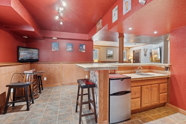 bar with sink, a textured ceiling, stainless steel refrigerator, track lighting, and wooden walls