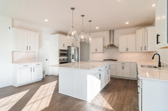 kitchen featuring wall chimney exhaust hood, sink, white cabinetry, a center island, and appliances with stainless steel finishes