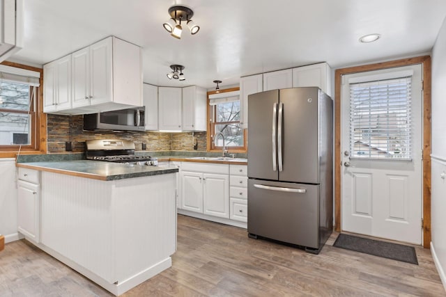 kitchen with sink, white cabinetry, light wood-type flooring, appliances with stainless steel finishes, and backsplash