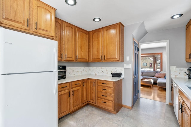 kitchen featuring baseboards, light countertops, recessed lighting, freestanding refrigerator, and brown cabinetry