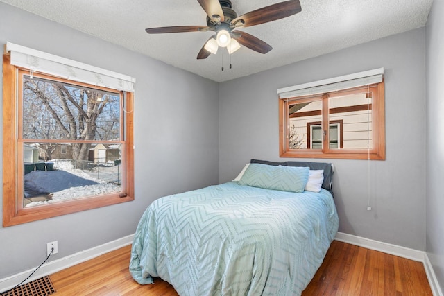 bedroom with a ceiling fan, visible vents, wood finished floors, baseboards, and a textured ceiling