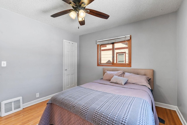 bedroom featuring wood finished floors, visible vents, baseboards, ceiling fan, and a textured ceiling