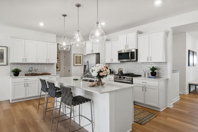 kitchen featuring pendant lighting, white cabinetry, a kitchen island with sink, and appliances with stainless steel finishes