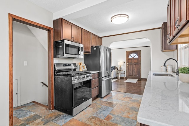 kitchen with sink, stainless steel appliances, a textured ceiling, and light stone countertops