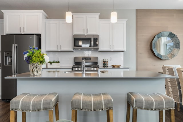 kitchen featuring appliances with stainless steel finishes, pendant lighting, white cabinetry, a breakfast bar area, and decorative backsplash