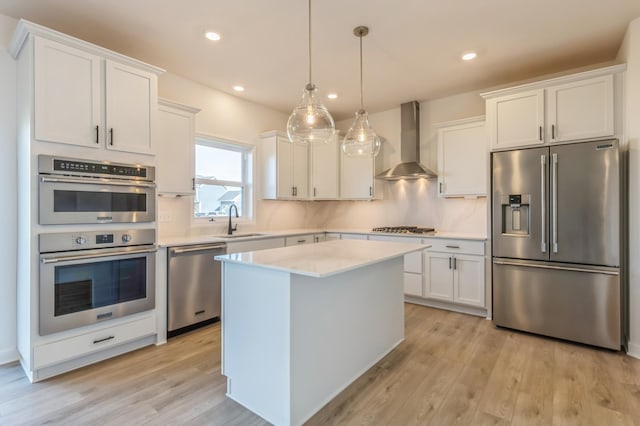 kitchen with white cabinetry, wall chimney range hood, decorative light fixtures, and stainless steel appliances