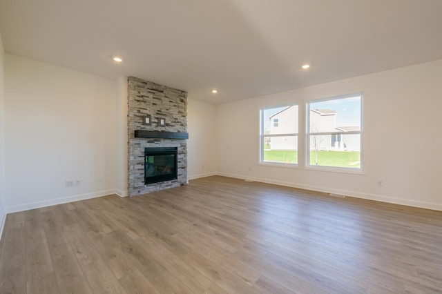 unfurnished living room with a stone fireplace and light hardwood / wood-style floors